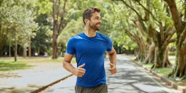 Man in blue shirt jogging down a tree lined street
